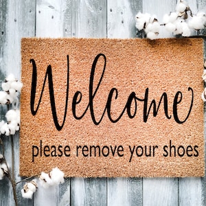 May include: Welcome doormat with the text "Welcome please remove your shoes" in black lettering on a brown background.