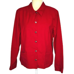 May include: A bright red button-down shirt with long sleeves and two front pockets. The shirt has a classic collar and is fastened with silver-toned buttons. The garment is displayed on a mannequin, showcasing its tailored fit and vibrant color.