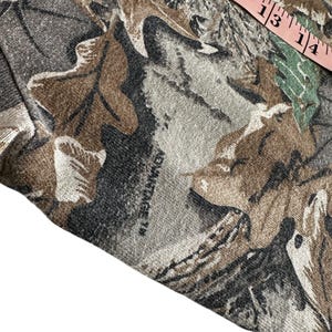 Puede incluir: Primer plano de una tela con estampado de camuflaje en tonos marr&oacute;n, gris y verde. La tela tiene un dise&ntilde;o de hojas con el texto "ADVANTAGE TM" visible. Una cinta m&eacute;trica rosa es parcialmente visible.