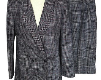 May include: A two-piece suit featuring a double-breasted blazer and a matching skirt. The suit is made of a plaid fabric in shades of gray, black, and red. The blazer has two black buttons and a notched collar.