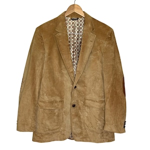 May include: A tan corduroy blazer with a notched lapel, two front pockets, and a two-button closure. The blazer has a patterned lining and elbow patches. It is hanging on a wooden hanger.