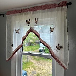 May include: Sheer white window curtains with embroidered rooster designs. The curtains have a red and white gingham trim and valance, adding a country kitchen aesthetic. The rooster embroidery is in shades of brown and black.