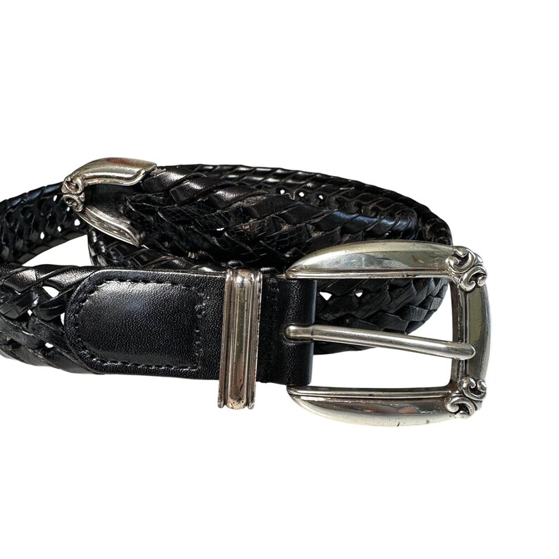 May include: Black leather belt with a woven design. The belt features a silver-colored buckle with decorative scrollwork. The belt is designed with a classic style and is suitable for various outfits.