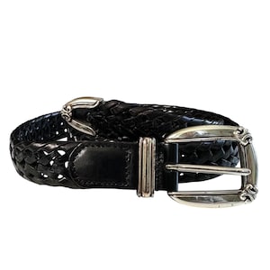May include: Black woven leather belt with a silver-toned buckle and keeper. The belt features a braided design and a rectangular leather tab near the buckle. The buckle has an ornate design.