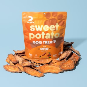 May include: A bag of Davie's Sweet Potato Dog Treats. The bag is orange and features a paw print and the text "Sweet Potato Dog Treats - Just One Ingredient - 100% Natural". The bag is surrounded by a pile of sweet potato dog treats.
