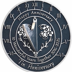Könnte beinhalten: Eine kreisförmige, dunkelgraue Sonnenuhr mit silbernem Rand und Gnomon. Sie zeigt römische Ziffern, den Text "Happy Anniversary", "10 Wonderful Years Together 2016-2026" und "Tin Anniversary" sowie eingravierte Blumen- und Glockenmotive.