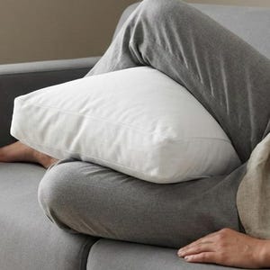 May include: A gray sofa with a white pillow. The sofa has a simple design and is upholstered in a neutral gray fabric. The white pillow provides a contrast to the sofa's color.