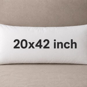 May include: A rectangular white pillow featuring the text 20x42 inch printed in black across the center. The pillow has a smooth, solid white fabric cover and a small dark blue tag visible on the bottom right corner of the item.