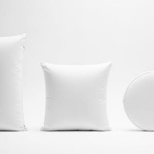 May include: Three white pillows of different shapes. A tall, rectangular pillow with a zipper, a square pillow, and a round pillow. All are plain white and appear to be made of soft fabric.
