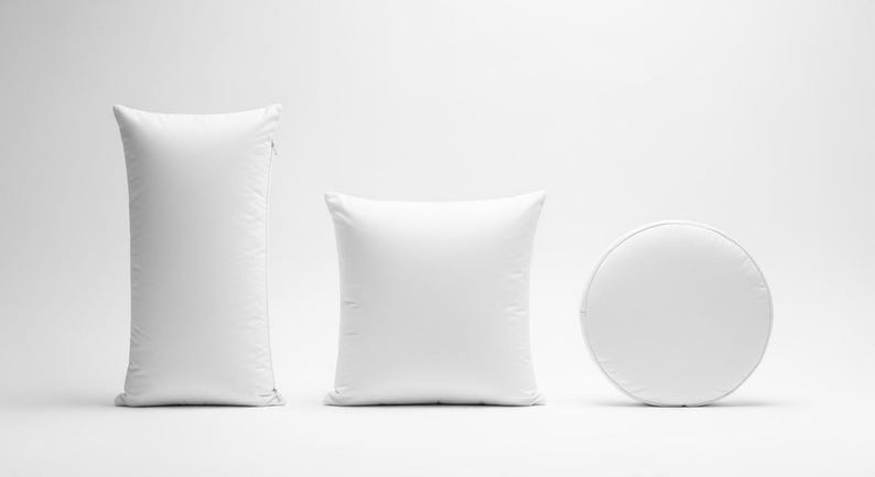 May include: Three white pillows of different shapes. A tall, rectangular pillow with a zipper, a square pillow, and a round pillow. All are plain white and appear to be made of soft fabric.