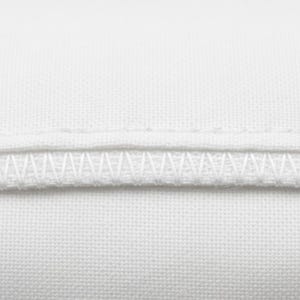 May include: Close-up of white fabric with two rows of stitching. The top row is a straight stitch, and the bottom row is a zigzag stitch. The fabric appears to be a tightly woven cotton or linen.