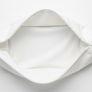 May include: A white, open, rectangular pouch with a zipper closure. The interior is also white, and the pouch is empty. The pouch is made of a soft, smooth material.