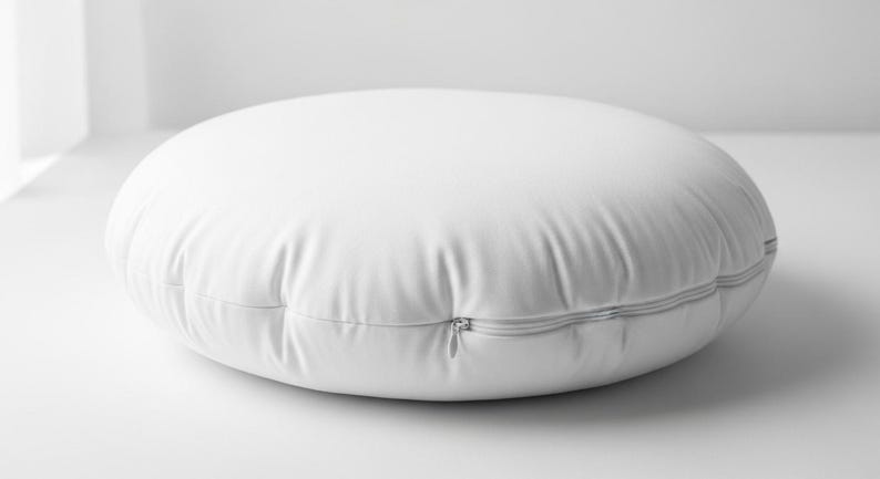 May include: A white, round floor pillow with a zipper closure. The pillow is made of a smooth, possibly synthetic material. The pillow is approximately 24 inches in diameter.