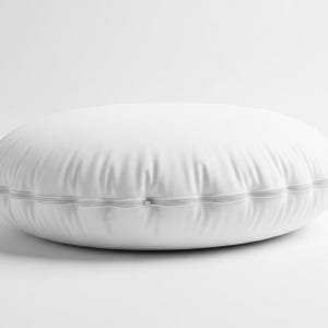 May include: A white, round floor pillow with a stitched edge. The pillow is made of a smooth, possibly leather-like material. The pillow is approximately 24 inches in diameter.