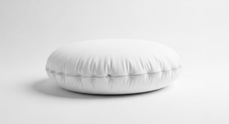 May include: A white, round floor pillow with a stitched edge. The pillow is made of a smooth, possibly leather-like material. The pillow is approximately 24 inches in diameter.