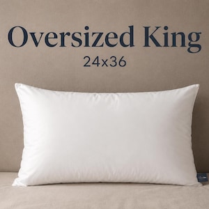 May include: A rectangular white pillow with a smooth surface. The text above the pillow reads Oversized King 24x36. The pillow features a small dark blue tag on the bottom right corner. The overall design is simple and functional for bedding.