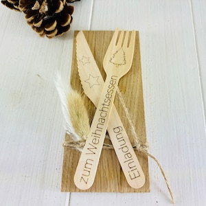 K&ouml;nnte beinhalten: Holzbesteck-Set mit einem Weihnachtsbaum-Design und dem Text "Zum Weihnachtsessen Einladung" auf einem Holzgrund.