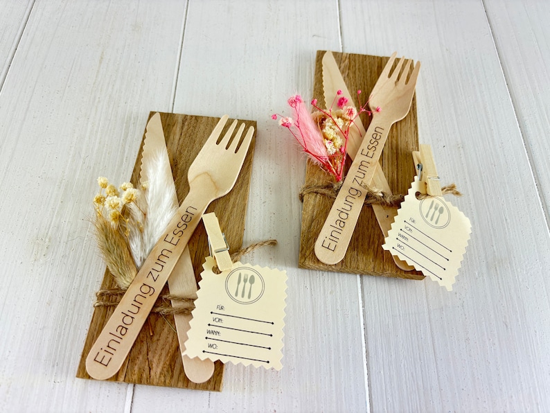 K&ouml;nnte beinhalten: Zwei Holz-Einladungen mit einem Messer und einer Gabel, die &uuml;bereinander gelegt sind. Die Einladungen sind mit Schnur gebunden und haben ein kleines Etikett mit den Worten "Einladung zum Essen" angebracht.