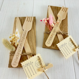 K&ouml;nnte beinhalten: Zwei Holz-Platzkarte mit je einer Gabel und einem Messer. Die Platzkarte sind mit getrockneten Blumen und Schnur verziert. Der Text auf den Platzkarte lautet "Einladung zum Fr&uuml;hst&uuml;ck".
