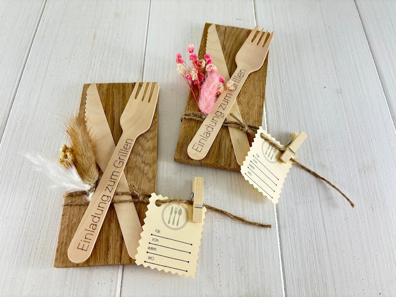 K&ouml;nnte beinhalten: Zwei Holz-Einladungen zum Grillen, jede mit einem Holz-Messer und einer Holz-Gabel, mit Schnur gebunden und mit getrockneten Blumen verziert. Die Einladungen sagen "Einladung zum Grillen".