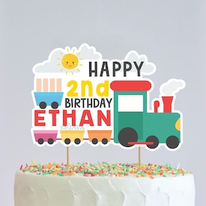 Op de afbeelding: Een kleurrijke trein caketopper met een zon, wolken en de tekst "Happy 2nd Birthday Ethan".