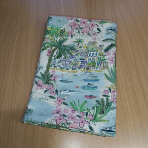 Peut inclure: Un tissu bleu et blanc avec une illustration colorée d'une ville côtière avec des bateaux et des palmiers. Le tissu présente des fleurs roses et des feuilles vertes.
