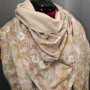 May include: A floral print scarf with a cream-coloured cowl neck. The scarf features a pattern of pink, yellow, and white flowers on a light green background. The cowl neck is made of a soft, cream-coloured fabric.