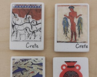 May include: Four white ceramic tiles with images of Minoan art from Crete. The tiles feature a red and white image of a bull, a red and blue image of a man holding fish, a blue and white image of dolphins, and a red image of a vase with a labyrinth design. Each tile has the word "Crete" written in black at the bottom.
