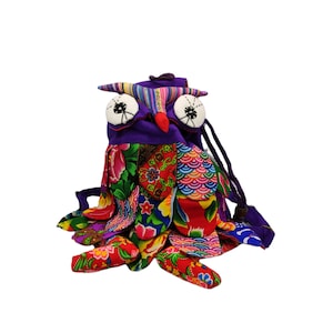 Może przedstawiać: Kolorowa torba ze sznurkiem w kształcie sowy wykonana z tkaniny patchworkowej. Torba ma fioletowe ciało z czerwonym dziobem i dużymi czarnymi oczami. Skrzydła i ogon wykonane są z różnych kolorowych tkanin z kwiatowymi i geometrycznymi wzorami.