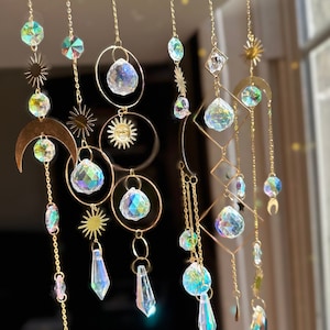 May include: A gold-toned crystal suncatcher with multiple iridescent crystal prisms hanging from chains. The suncatcher features a crescent moon, sun, and star shapes.