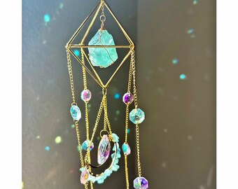 May include: A gold geometric crystal mobile with a large light blue crystal hanging from the center. The mobile has multiple strands of gold chains with iridescent beads and crystals.