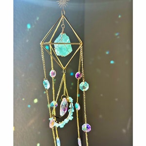 May include: A gold geometric crystal mobile with a large light blue crystal hanging from the center. The mobile has multiple strands of gold chains with iridescent beads and crystals.
