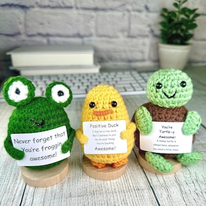 May include: Three crocheted amigurumi figures: a green frog, a yellow duck, and a green turtle. Each holds a sign with an inspirational message. The frog says, "Never forget that You're froggin awesome!" The duck says, "Positive Duck...You're Ducking Awesome!" The turtle says, "You're Turtle-y Awesome!"