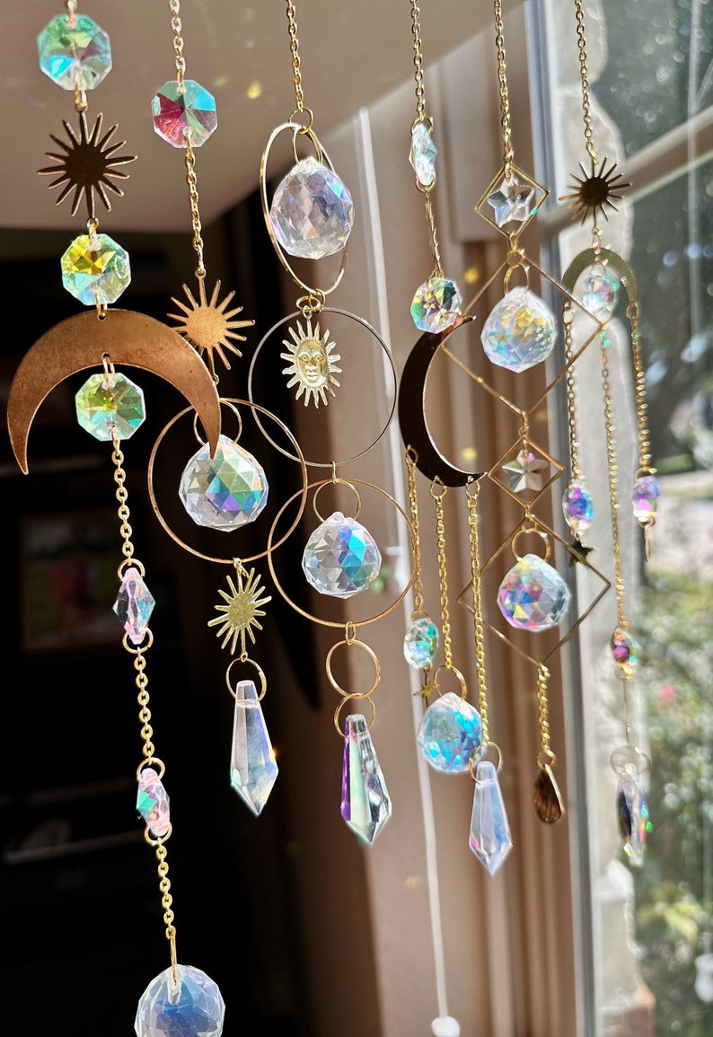 May include: A gold-toned metal sun and moon mobile with iridescent crystal beads and teardrop-shaped prisms. The mobile features a crescent moon, a sun with a face, and stars.
