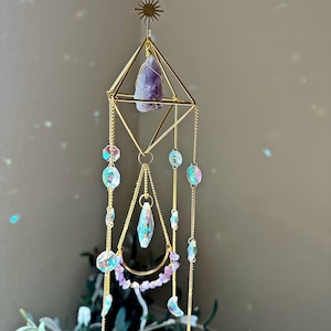 May include: A gold geometric crystal suncatcher with a purple amethyst crystal, iridescent glass beads, and gold chains.