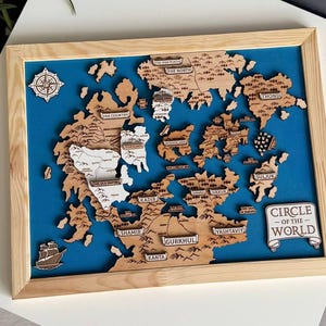 May include: Wooden world map art piece with a blue background, framed in light wood. The map features detailed cutouts of continents and islands, with labeled locations. A compass rose and a ship are included in the design. The text "CIRCLE OF THE WORLD" is visible.
