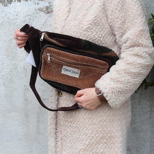 May include: A brown and green corduroy fanny pack with a brown strap and a white label that says "Tartan Threads".