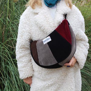 May include: A corduroy shoulder bag with a patchwork design in shades of brown, gray, black, and burgundy. The bag has a curved shape and a small handle. The text "Queen Cleo's" is on a white label.