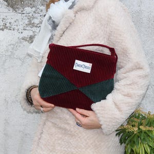 Może przedstawiać: Bordowa torebka sztruksowa z zielonym geometrycznym wzorem. Torba ma mały uchwyt i etykietę z napisem "Camden Threads". Torba jest trzymana na tle jasnego, teksturowanego tła.