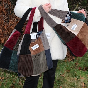 May include: Several corduroy tote bags in a variety of colours, including black, burgundy, brown, and green. Each bag is patchwork style with a rectangular shape and a long strap. The bags have a label that reads "PureChic".