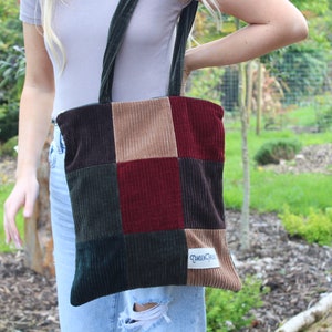 May include: A patchwork tote bag made of different colored corduroy fabric. The bag has a brown, tan, green, and burgundy color scheme. The bag has a label that says "Queen Creek".