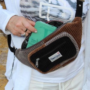 May include: A corduroy fanny pack in shades of brown, gray, and black. The bag has multiple compartments, including a zippered front pocket and a main compartment. A mint green wallet is visible inside. The label "Camden Threads" is on the front.