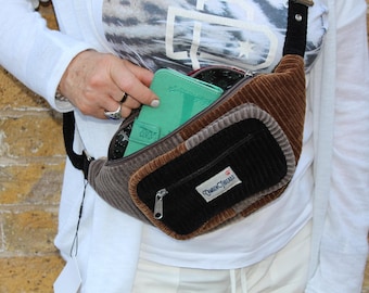 May include: A corduroy fanny pack in shades of brown, gray, and black. The bag has multiple compartments, including a zippered front pocket and a main compartment. A mint green wallet is visible inside. The label "Camden Threads" is on the front.