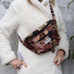 May include: A brown and black floral fanny pack with a zipped pocket and the text "Tonic Cloth" on the front.