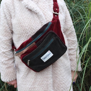 May include: A brown, green, and red corduroy fanny pack with a zipper closure and a "Queen Circus" label.