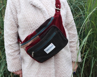 May include: A brown, green, and red corduroy fanny pack with a zipper closure and a "Queen Circus" label.