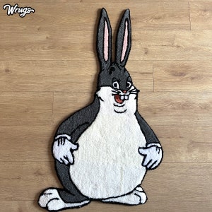 Op de afbeelding: Een zwart-wit pluche vloerkleed met een cartoon afbeelding van een groot, glimlachend konijn met een witte buik. Het vloerkleed is gemaakt van zacht, pluche materiaal en is perfect om elke kamer een vleugje whimsy te geven.
