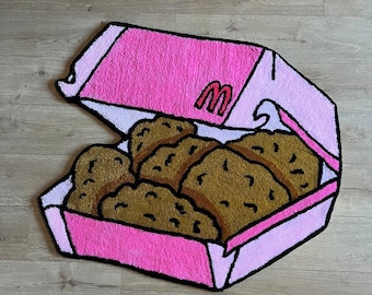May include: A pink rug shaped like a fast-food chicken nugget box, with the McDonald's logo visible. The rug features a box filled with brown, textured chicken nuggets. The word "Wrugs" is in the top left corner.
