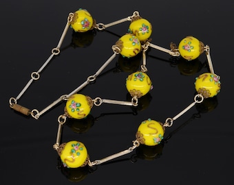 May include: A yellow glass necklace with floral designs and gold accents. The necklace is made of a silver chain with yellow glass beads.