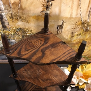 May include: A three-tiered corner shelf made of dark wood with a wood grain pattern. The shelf has a scalloped edge and is supported by four turned wooden legs.